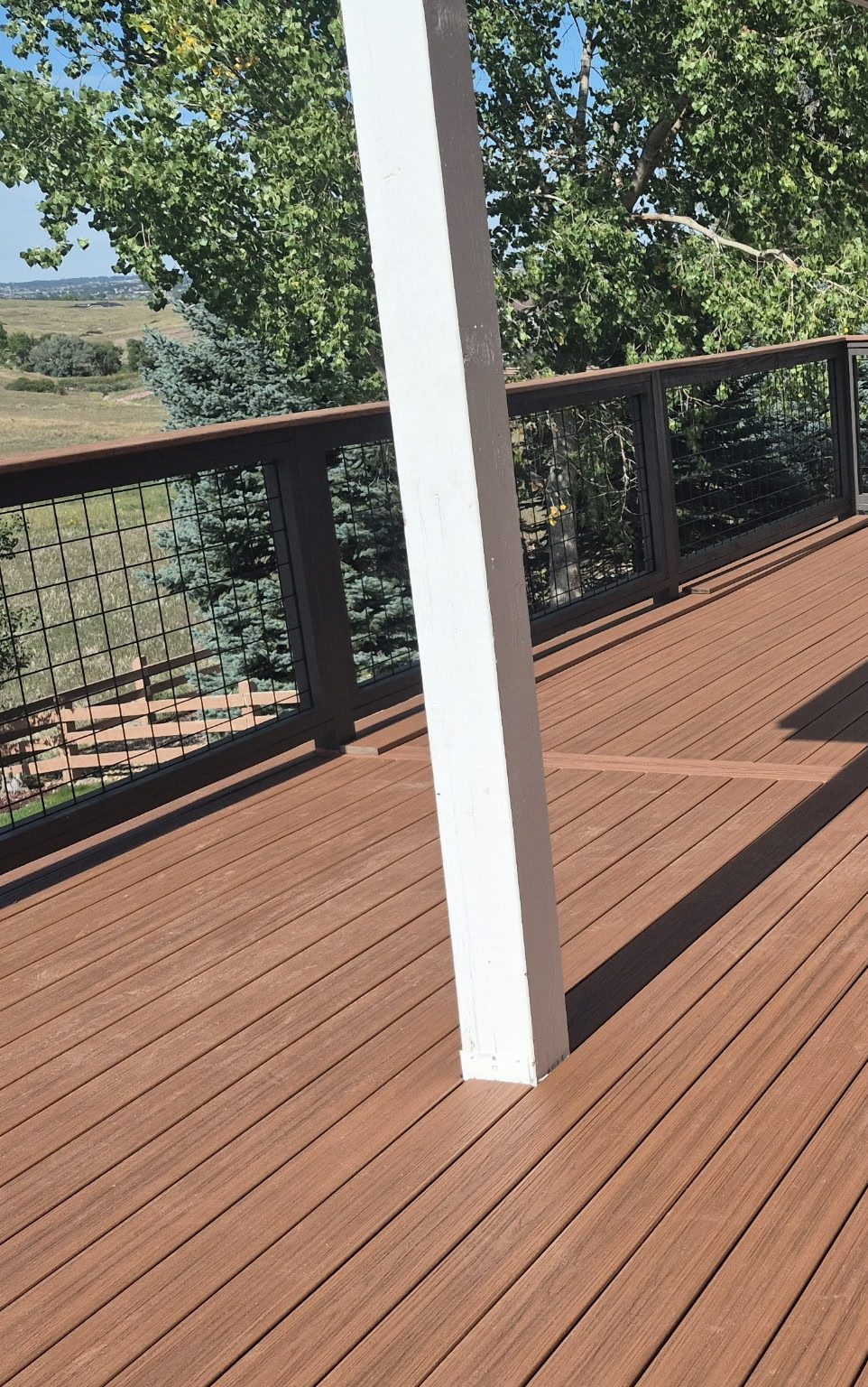 Composite deck with hog-wire railing and white posts under a covered patio