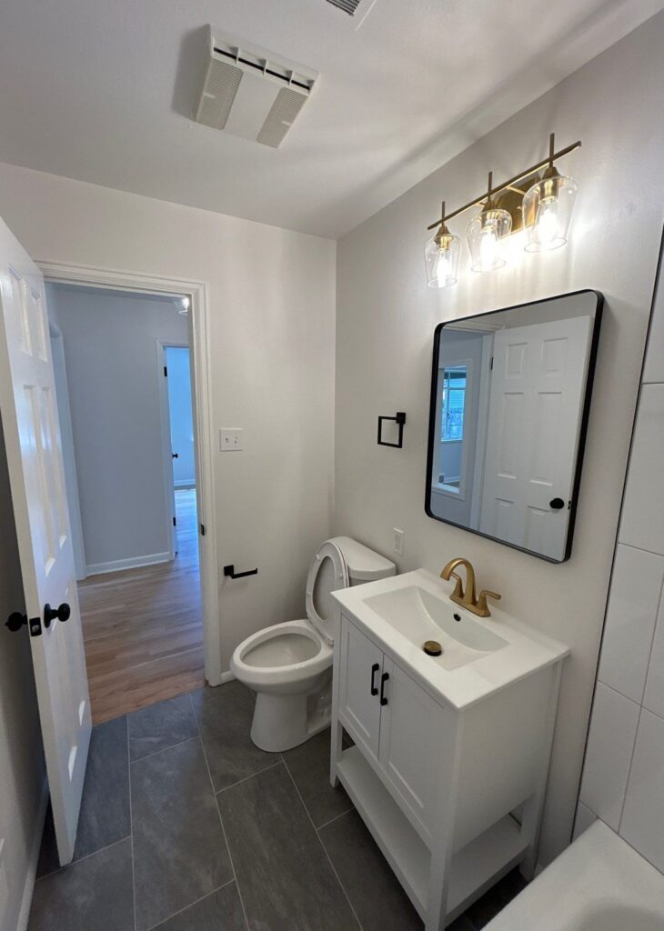 After: bathroom remodel with gold faucet, gold vanity light, black mirror and tile floor, Denver