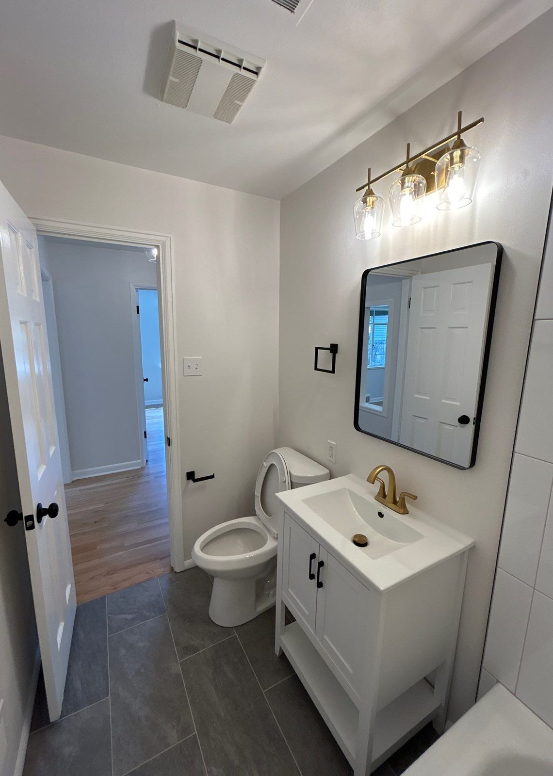 After: bathroom remodel with gold faucet, gold vanity light, black mirror and tile floor, Denver