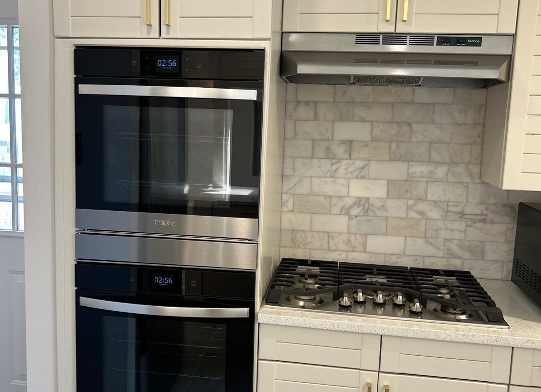 After: white cabinets with brass pulls, stainless double wall ovens, gas cooktop and marble subway backsplash, Denver kitchen remodel