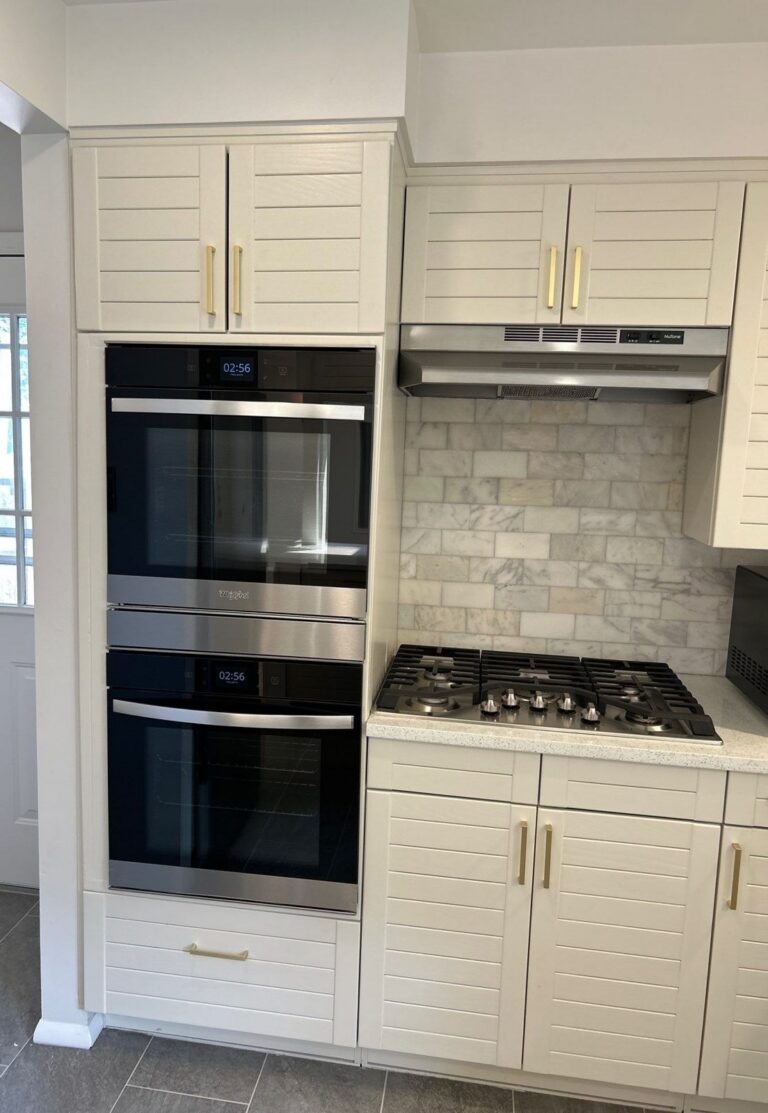 After: white cabinets with brass pulls, stainless double wall ovens, gas cooktop and marble subway backsplash, Denver kitchen remodel