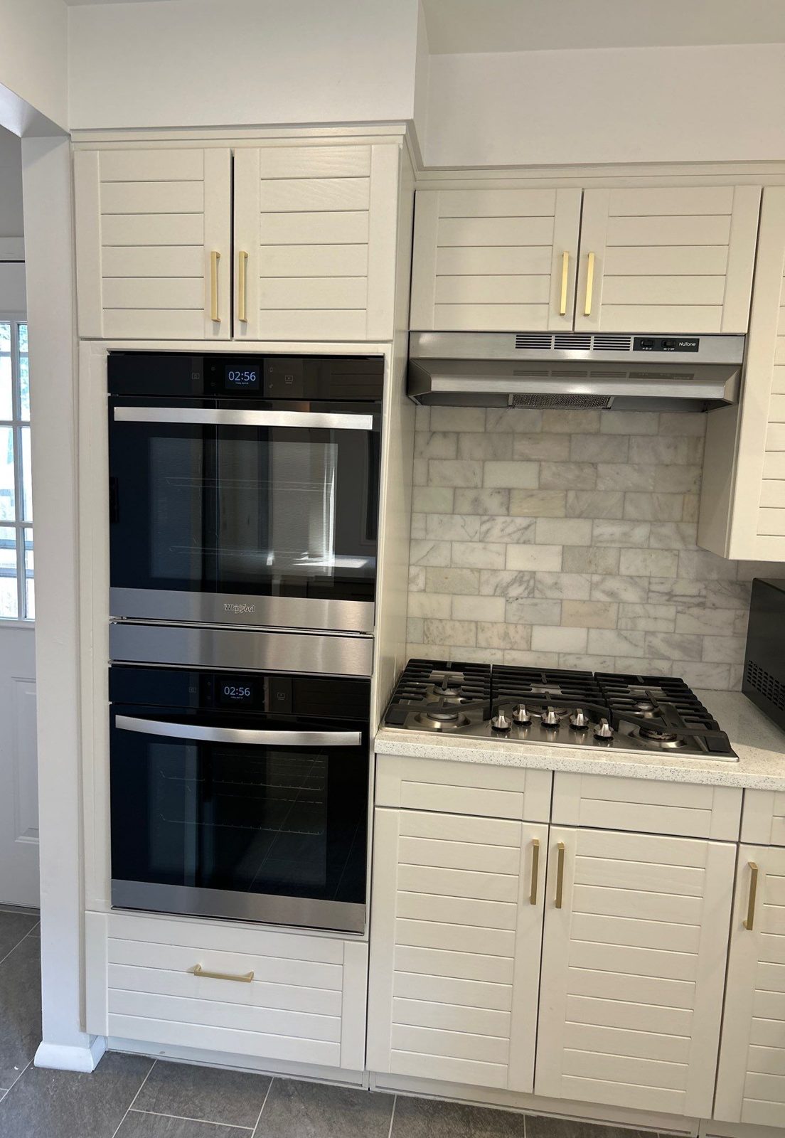 After: white cabinets with brass pulls, stainless double wall ovens, gas cooktop and marble subway backsplash, Denver kitchen remodel