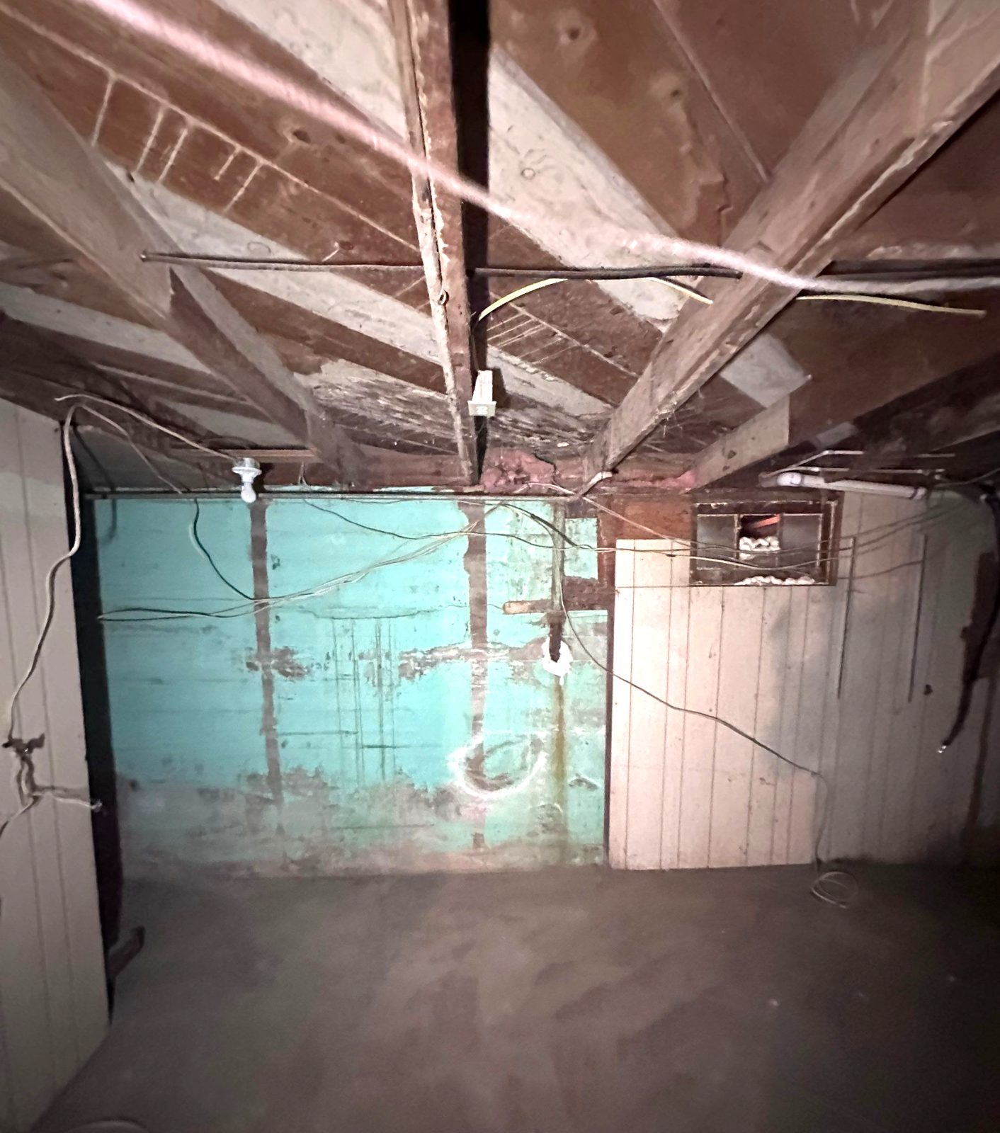 Before: cracked basement foundation wall with peeling teal paint and loose wiring, Fort Morgan