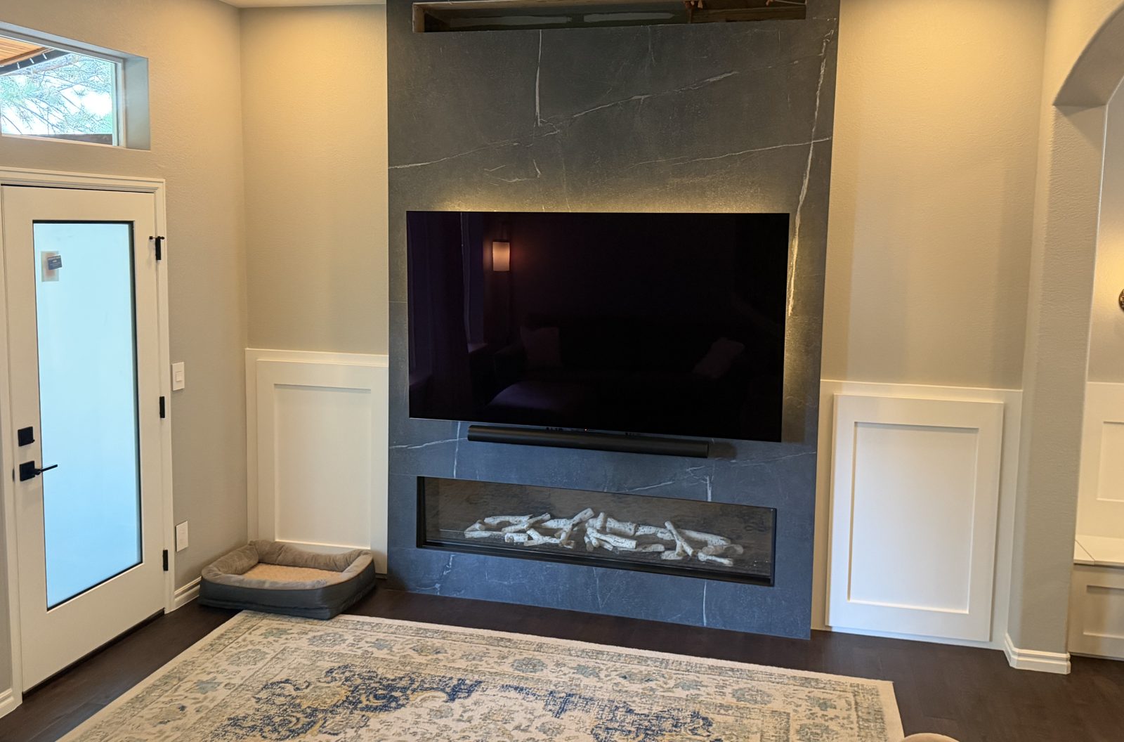 After: floor-to-ceiling stone-look slab fireplace wall with linear gas fireplace and paneled wainscot, Highlands Ranch