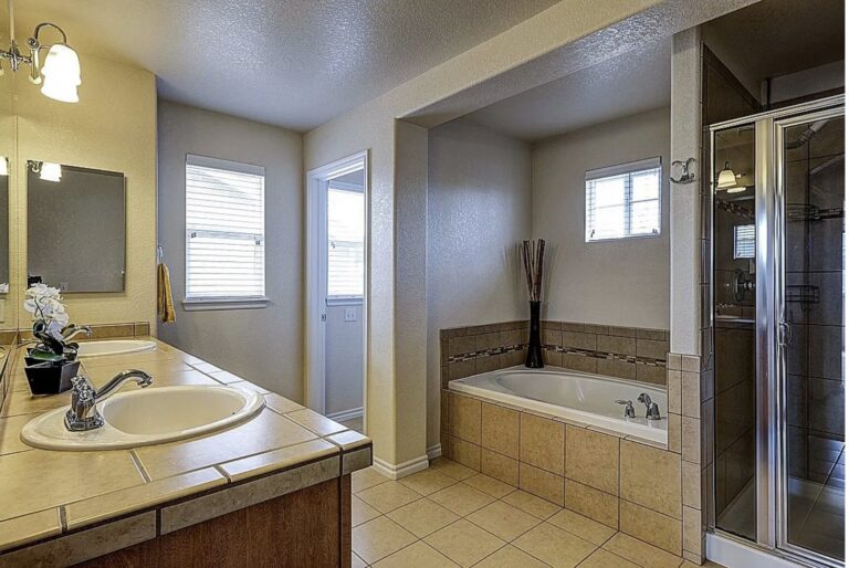 Before: primary bath with tiled drop-in tub, framed glass shower and tile-top double vanity, Highlands Ranch
