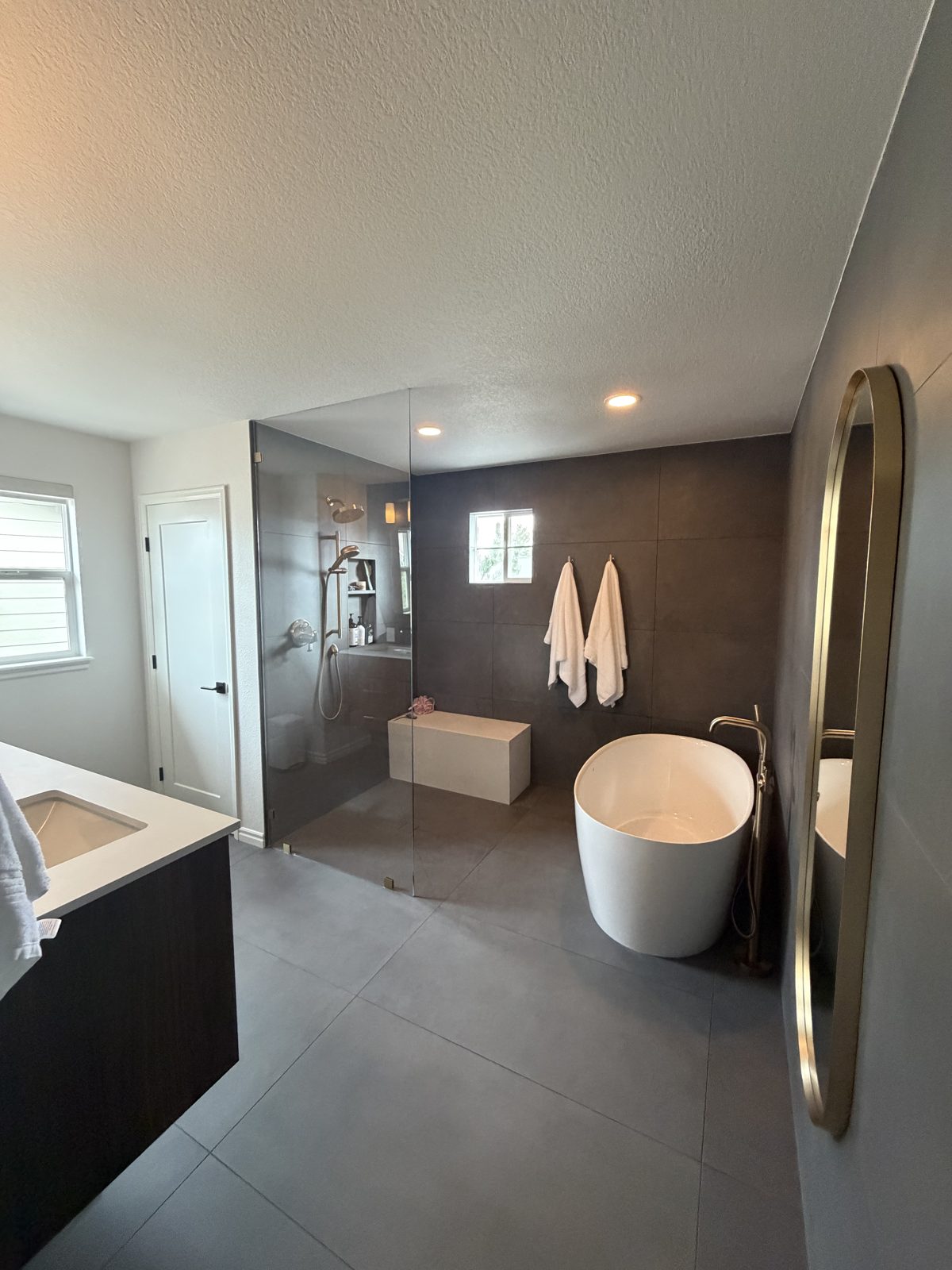 After: primary bath with freestanding tub, curbless glass walk-in shower, built-in shower bench and gold mirror, Highlands Ranch