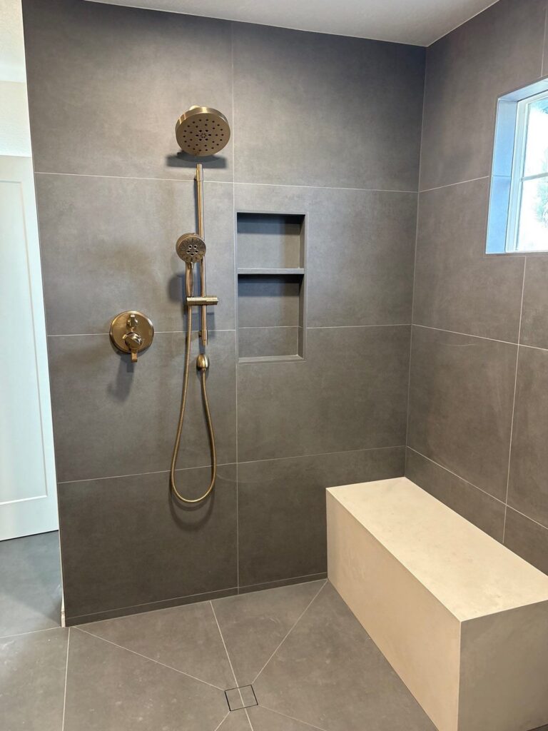 Highlands Ranch primary bathroom walk-in shower with gold fixtures and bench by Brimie Contractors