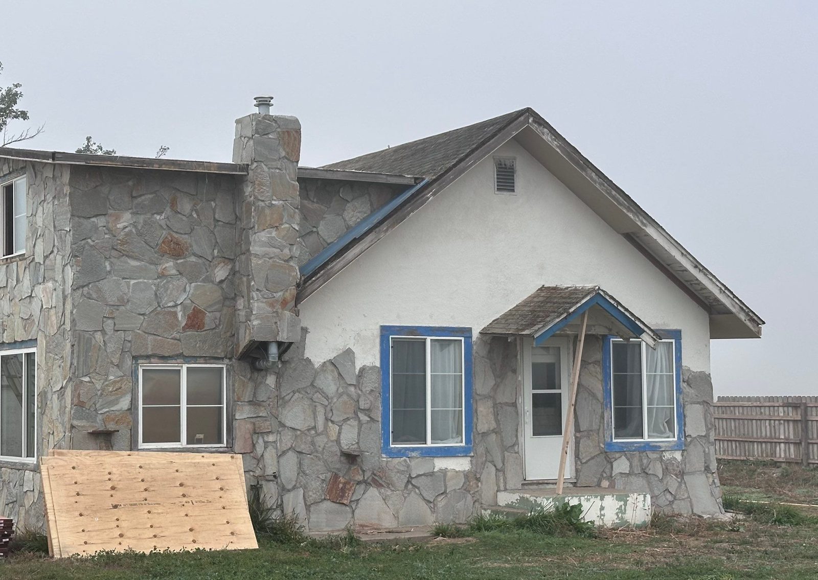 Before: stone and stucco farmhouse exterior with worn trim and old porch, Fort Morgan