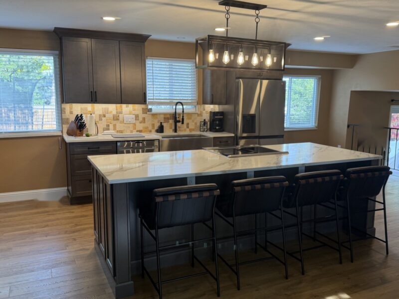 After: Littleton open kitchen with dark shaker cabinets, stone mosaic backsplash, farmhouse sink and a large marble-look quartz island with seating for four