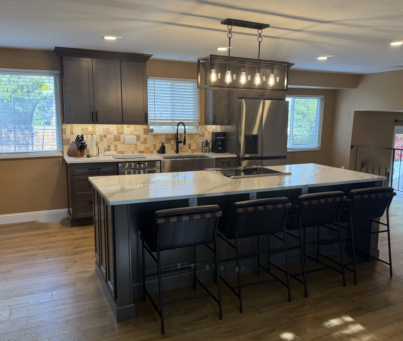 After: Littleton open kitchen with dark shaker cabinets, stone mosaic backsplash, farmhouse sink and a large marble-look quartz island with seating for four