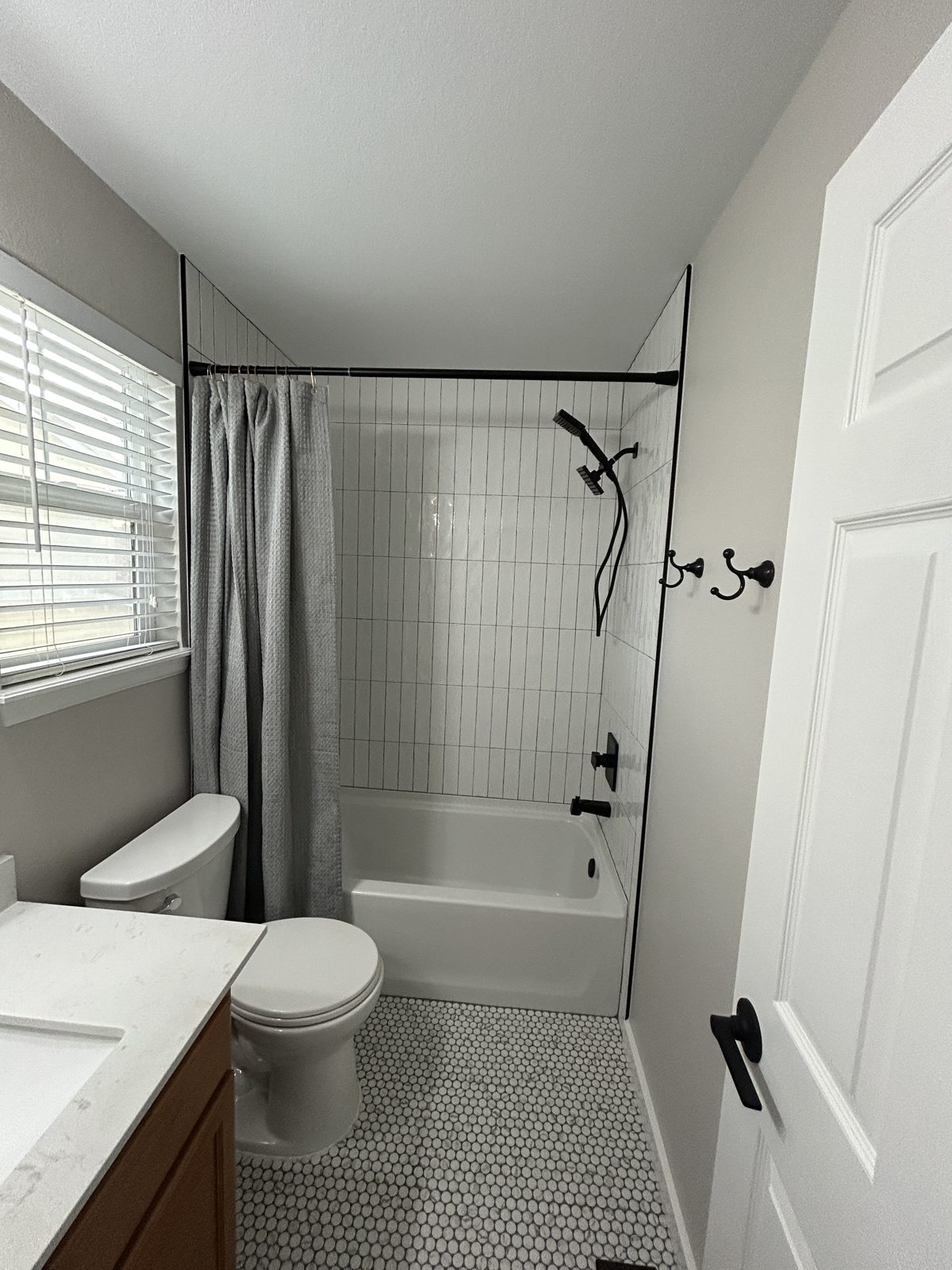 Parker hall bath remodel with white vertical tile, penny tile floor and matte black fixtures